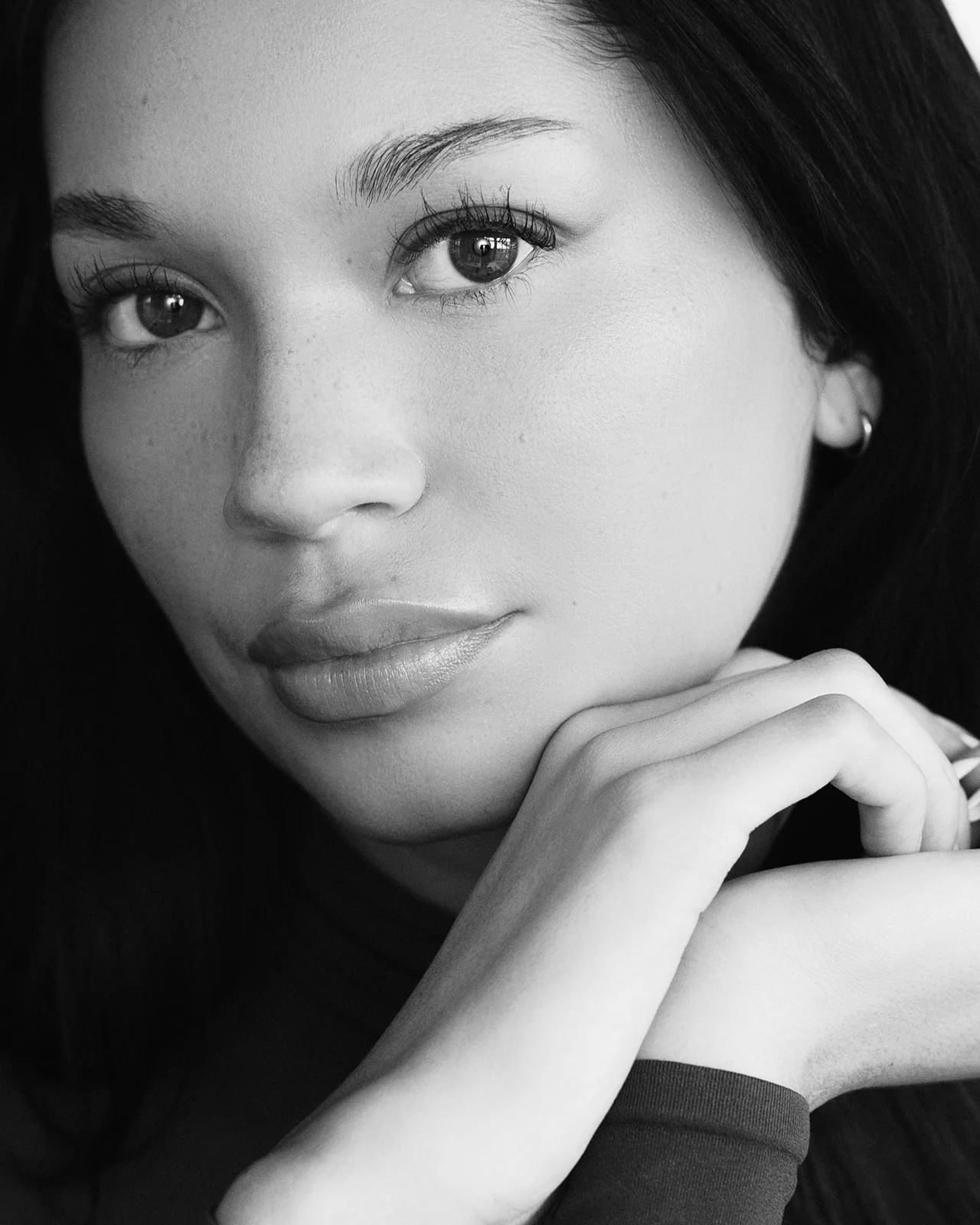 Black-and-white close-up of Kaila Triniti resting her chin on her stacked hands and looking into the camera.