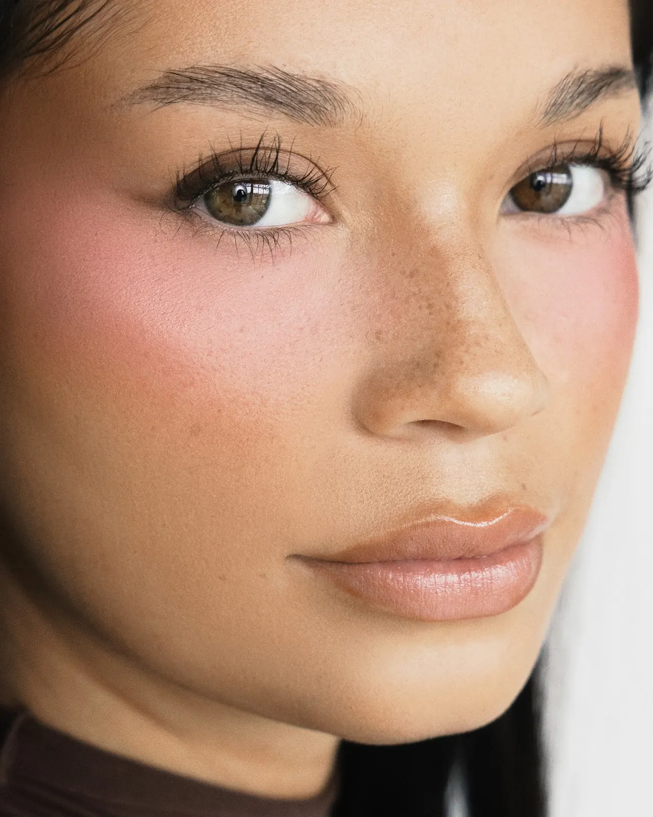 Close-up beauty portrait of Kaila Triniti looking straight into the camera, with natural freckles, rosy blush and glossy nude lips.